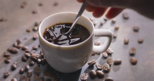 Stirring Dark Coffee in White Mug with Beans