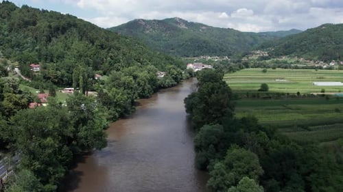 Aerial view of muddy river flowing through farmland and green hills