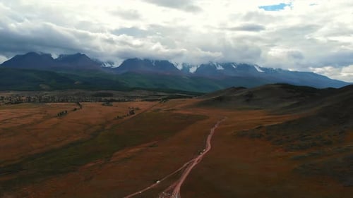 Cars Driving on a Dirt Road Towards Snow Capped Mountains Media