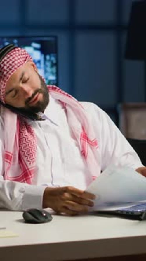 Man Wearing Headscarf Talking on Phone at Desk