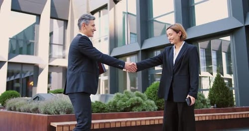 Business people colleagues man and woman shaking hands outdoors in financial district.