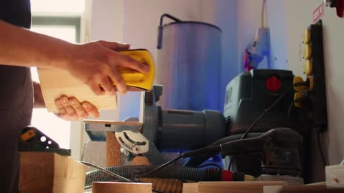 Craftsman Sands a Block of Wood in Workshop