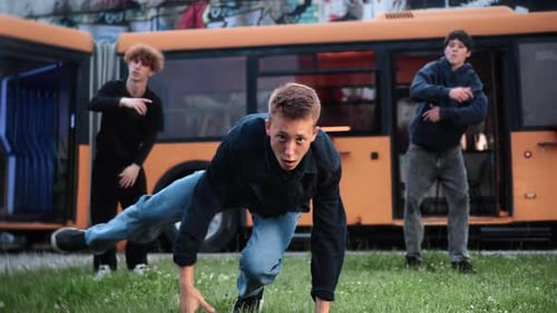 Breakdancers Practicing Highenergy Street Dance Moves Near Bright Orange Bus Representing Urban