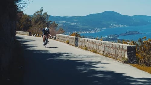 Cyclist rides on a mountain road among high mountains and ocean, a lone sportsman cycling on road
