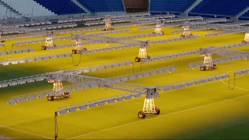 Row of grow lights on wheels illuminating grass in an empty football stadium, maintenance concept, e