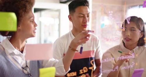 Felizes e diversificados colegas criativos masculinos e femininos discutindo ideias na parede de vidro, em câmera lenta