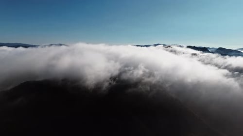 Breathtaking Aerial View of Clouds Draping Mountain Peaks at Dawn
