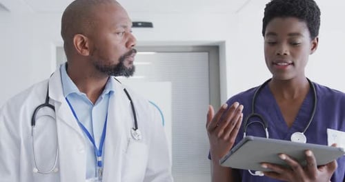 African american male and female doctors using tablet, talking at hospital