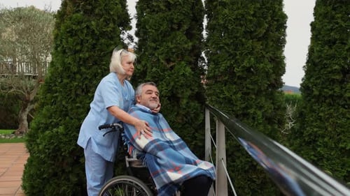Nurse comforting elderly man in wheelchair in a garden