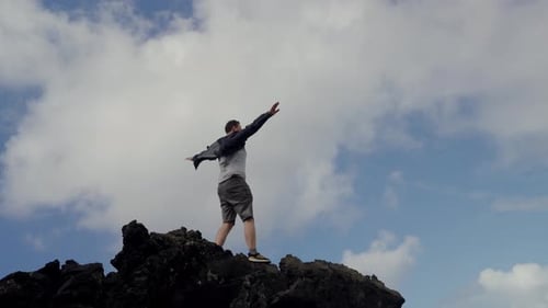 Man Standing on Cliff with Raised Hands Feeling Freedom and Enjoying Nature