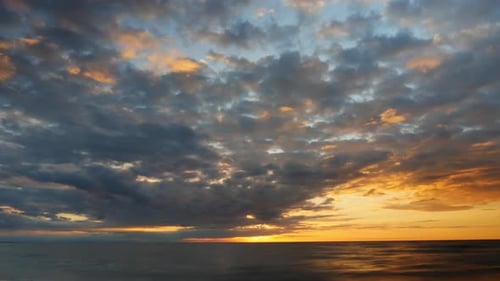 Time lapse sunset over the sea, sky with dark clouds. Low angle, long shutter speed 4K UHD 3840x2610