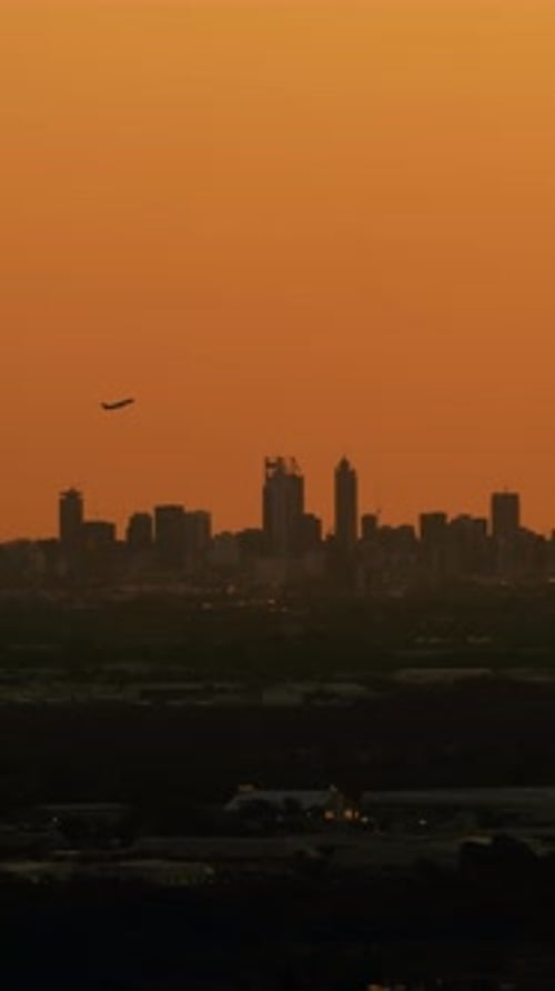 Jet departing with urban skyline at sunset