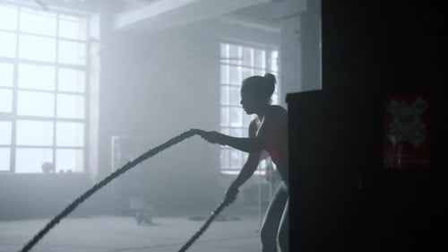 Female Bodybuilder Doing Battle Ropes Exercise in Cross Fit Gym. African American