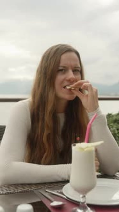 A young woman drinks a cocktail in a restaurant on a mountain by the sea. Vertical video Social Medi