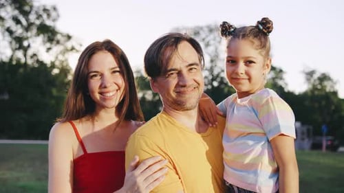 A Family Stands Together in a Park Embracing Each Other with Smiles on Their Faces The Sunlight