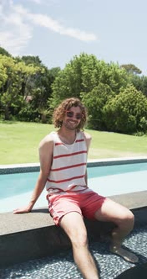 Vertical video: Caucasian young man sitting by pool, smiling, at home