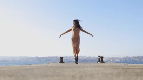 A Dancing Woman is on a Dock By the Water Wearing a Dress and Boots