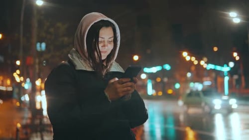 Young Pretty Woman Text Messaging on Her Smart Phone in City Street at Night