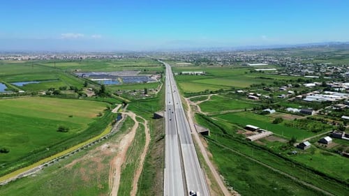 Aerial view of a busy highway cutting through lush green fields, with cars and trucks in motion.