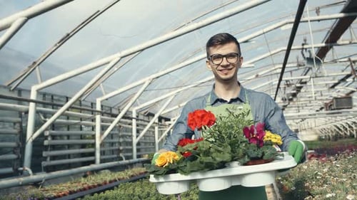 Smiling Man Holding Pot with Flowers in a Garden Center