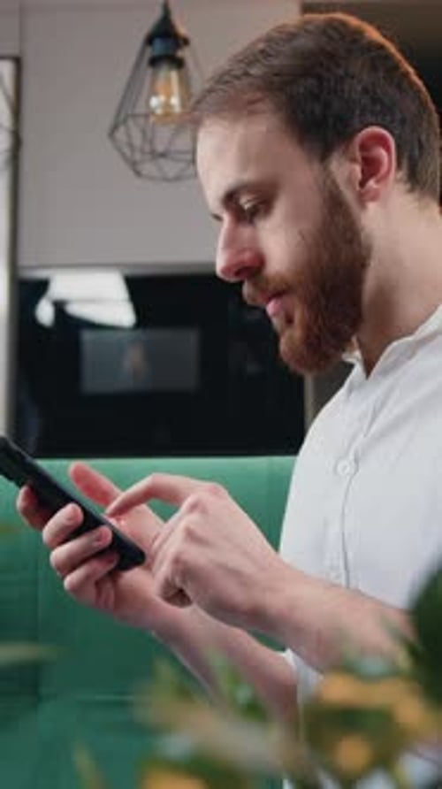 Man with Beard Using Smartphone in Modern Interior