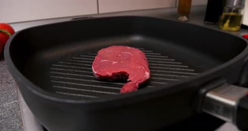 Close up shot of a delicious steak in the hot pan during searing in a kitchen in slow motion