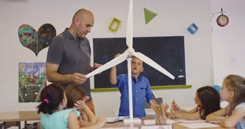 Elementary School Teacher Explaining Wind Turbine Model to Curious Children in Classroom STEM Lesson