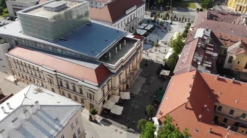 Ascending drone shot over a small city square with a big glass house on top of a building