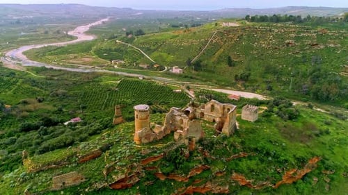 Aerial forwarding shot of ruins of an old building over hilly terrain with a winding river flowing i