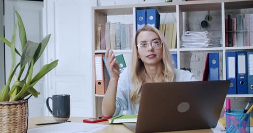 Blonde Young Businesswoman Sitting By Laptop in the Office Talking at Camera Explaining Work or