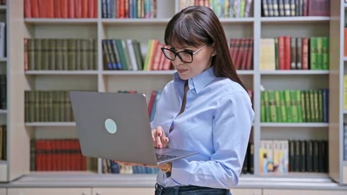 Porträt einer selbstbewussten Lehrerin, die einen Laptop in der Bibliothek benutzt und lächelt und in die Kamera blickt