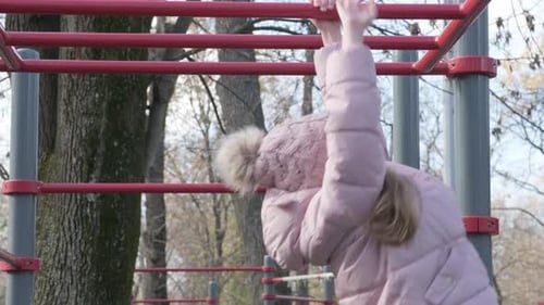 School Girl Climbs on Horizontal Bars on the Playground in Autumn Park
