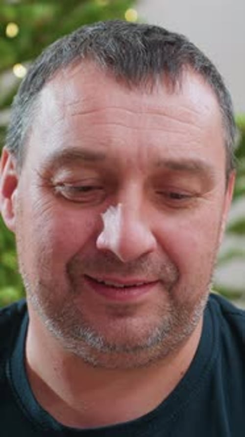 Man Smiling Holding Ornament in Front of Tree
