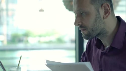 Young Man Working with Documents and Laptop in Cafe 30s
