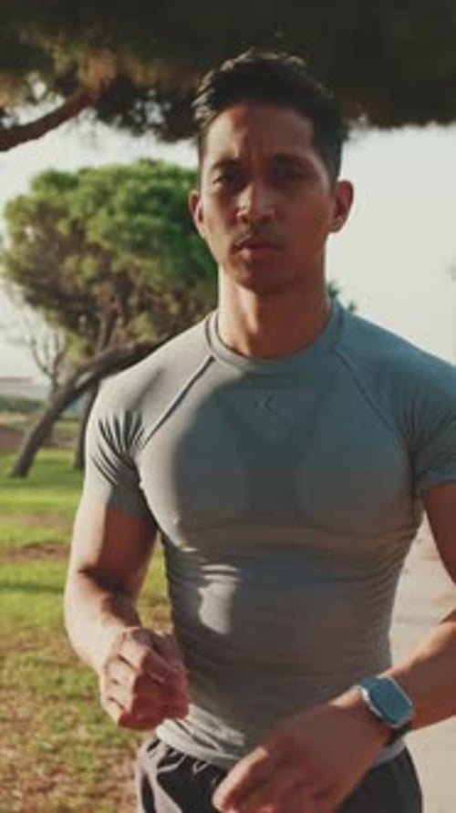Young man walks along a path in the park and looks at his smart watch