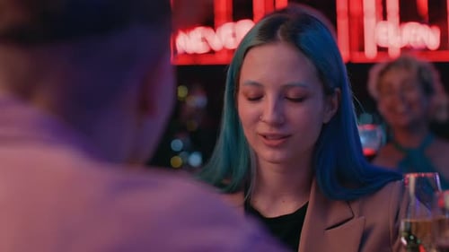 Smiling girl at romantic date talks to man in neon light at night club bar
