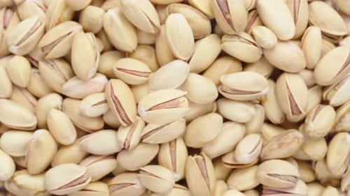 One salted pistachio rotates on a background of pistachios. Close-up.