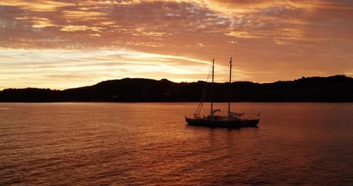 Aerial view of a sailing boat at sunset in the middle of the pristine sea.