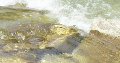 Crystal-clear drinking water flows between stones of a river or stream