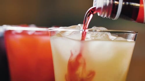 Process Making Cocktails. Batender pours Red Syrup into a yellow cocktail. Close Up Slow Motion