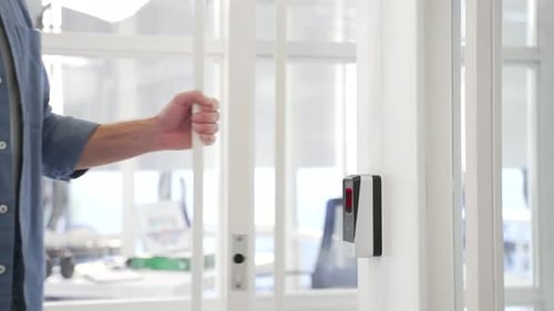 Close up of a man's hand opening a glass office door holding a doorknob in a modern business center.