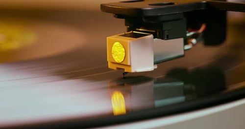 Detailed close-up of a turntable tonearm with white cartridge headshell, positioned over a black