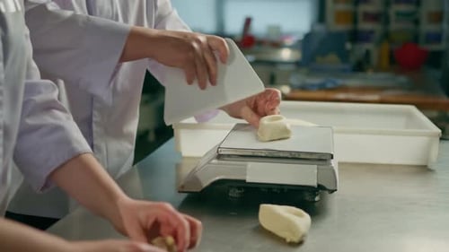 two bakers shape the raw dough before baking, cut it and roll it out on table professional kitchen