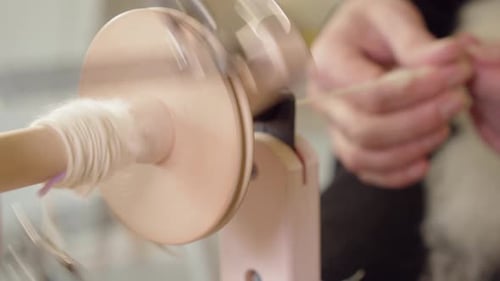 Select focus closeup: Spinning bobbin foreground, hands in background