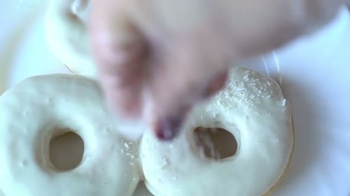 Cheftechnologe streut Kokosflocken auf frisch glasierte Donuts aus nächster Nähe