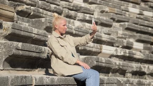 Woman is Sitting on the Steps of an Ancient Amphitheater and Taking Pictures