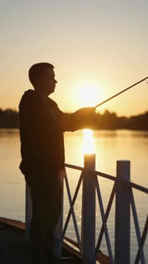 Mann fischt bei Sonnenuntergang auf dem Pier Konzept des Fischens