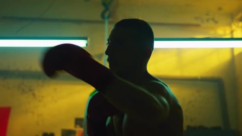 Shirtless Man Boxing in Dimly Lit Gym