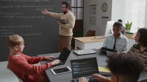 Männlicher Programmierlehrer erklärt verschiedenen Schülern Programmierprinzipien