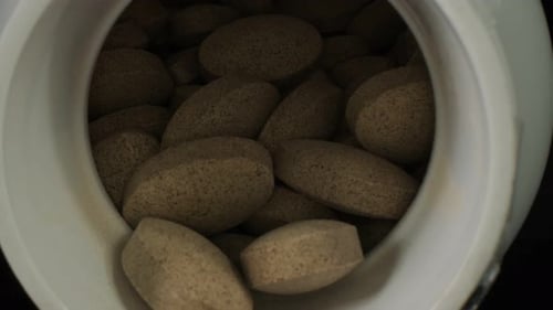 Pills in a White Plastic Jar on a Dark Background